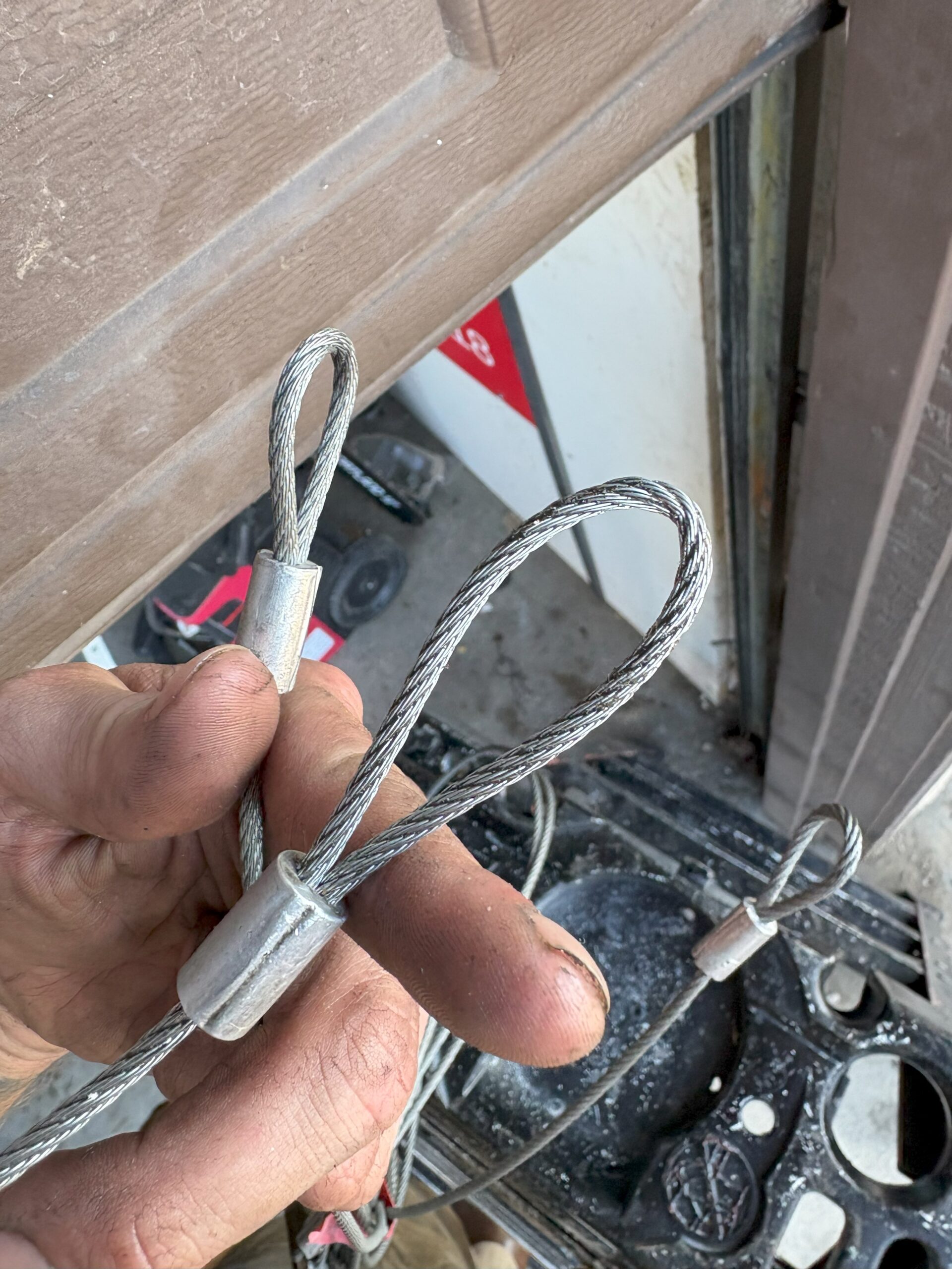 A hand holds three steel cables with looped ends, showcasing their sturdy metal terminals against a blurred background.